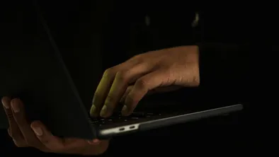 Мужчина держит ноутбук в темноте