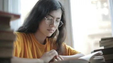 Девушка в очках сидит над учебниками