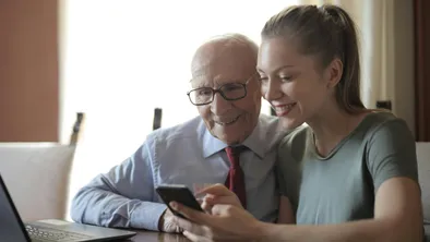 Пожилой мужчина и девушка смотрят в телефон и улыбаются
