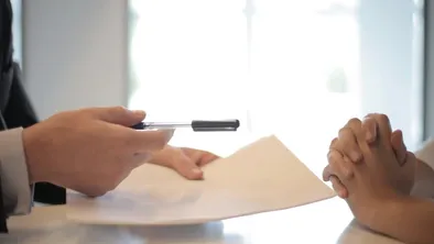 руки двух человек и листы бумаги, один человек протягивает второму ручку
