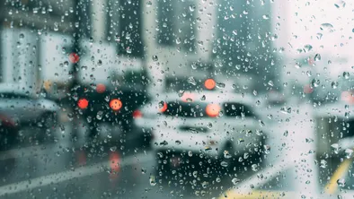 Вид на дорогу с едущими автомобилями через оконное стекло с каплями дождя