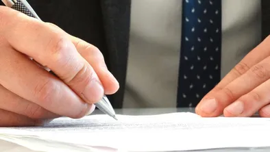 Мужчина подписывает документ ручкой
