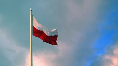 Флаг Польши на флагштоке на фоне неба с облаками